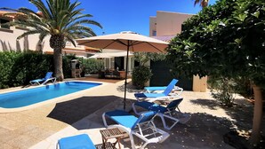 A pool area with two pools, lounge chairs, umbrellas, and a palm tree.