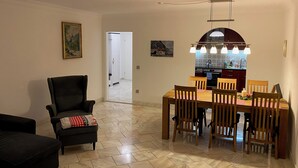 Ein Essbereich mit einem Holztisch und Stühlen, einem schwarzen Sessel und einer Küche im Hintergrund.