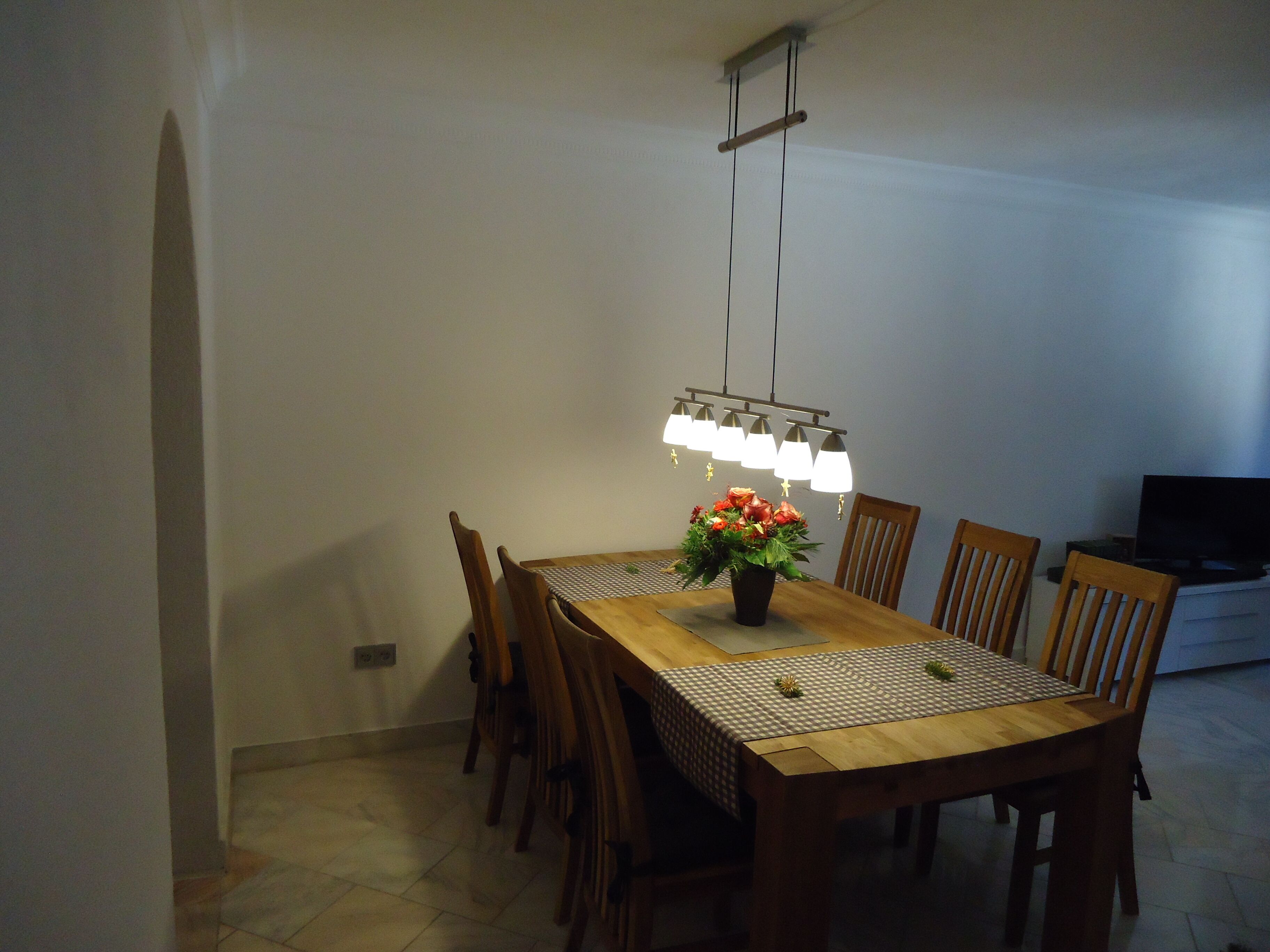 A dining area with a wooden table, chairs, a chandelier, and a potted plant.