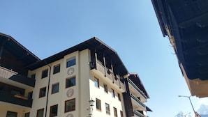 Ein mehrstöckiges Gebäude mit Balkonen, eine Straße davor und Berge im Hintergrund.