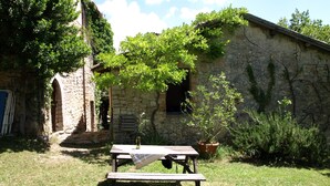 A stone building with ivy, a wooden bench, and a table with a bottle.