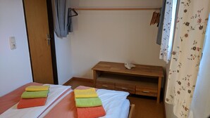Ein Schlafzimmer mit zwei Betten, einem Holznachttisch, einem Kleiderhaken und einem Fenster mit blumigen Vorhängen.