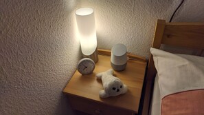 A wooden bedside table with a white lamp, a clock, and a plush toy.