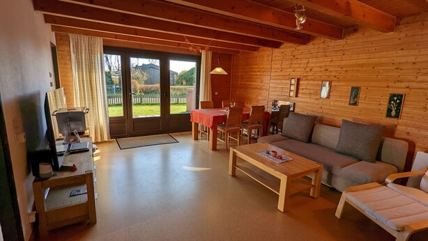 Ein gemütliches Zimmer mit Holzvertäfelung, einem Esstisch, einer Couch und einem Fernseher.