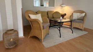 Una habitación con mobiliario de mimbre, una mesa de centro de vidrio, un espejo y una lámpara.