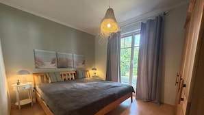 Un dormitorio con una cama grande, dos mesitas de noche, una lámpara colgante, una ventana con cortinas y una obra de arte en la pared.