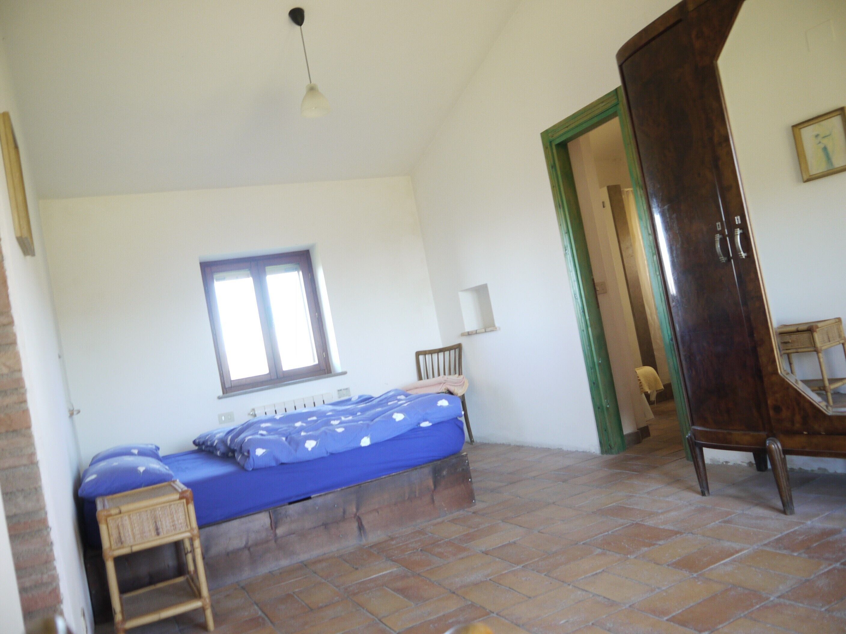 A bedroom with a bed, a window, a wardrobe, and a chair.