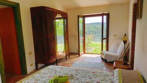 Un dormitori amb un llit, una cadira, un armari i vista a vegetació a través de la finestra.