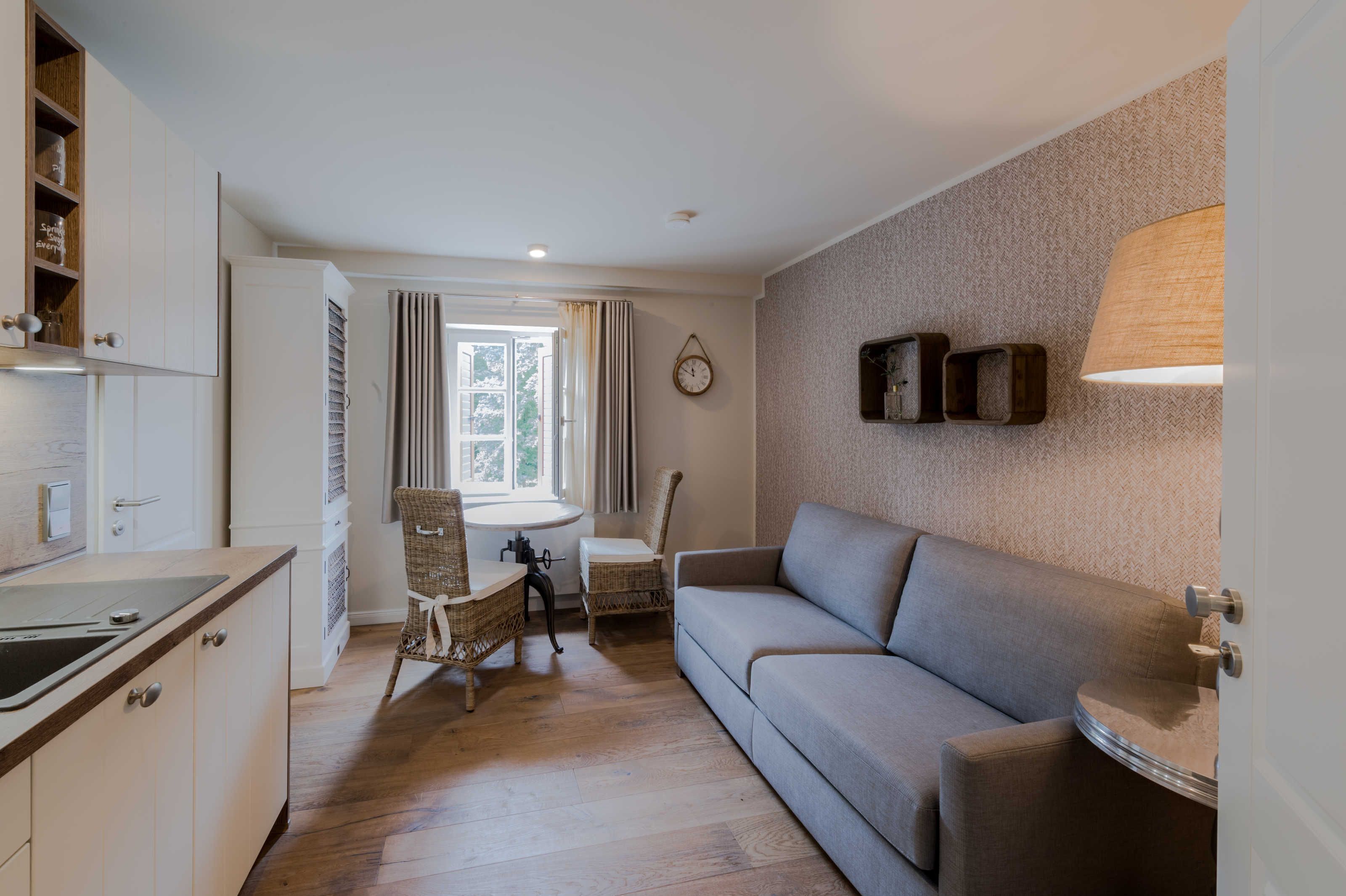 Ein kompakter Wohnraum mit Küchenzeile, einem Essbereich mit Korbstühlen, einer Couch und einer Wandlampe.