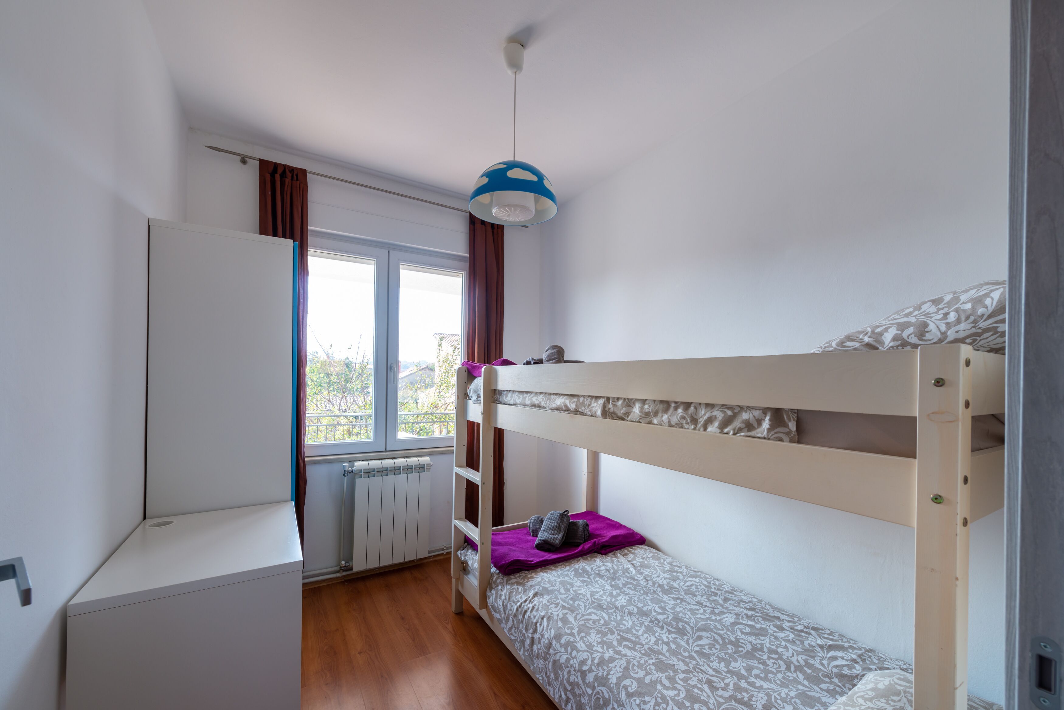 Une chambre de dortoir avec un lit superposé, un bureau et une fenêtre avec des rideaux.
