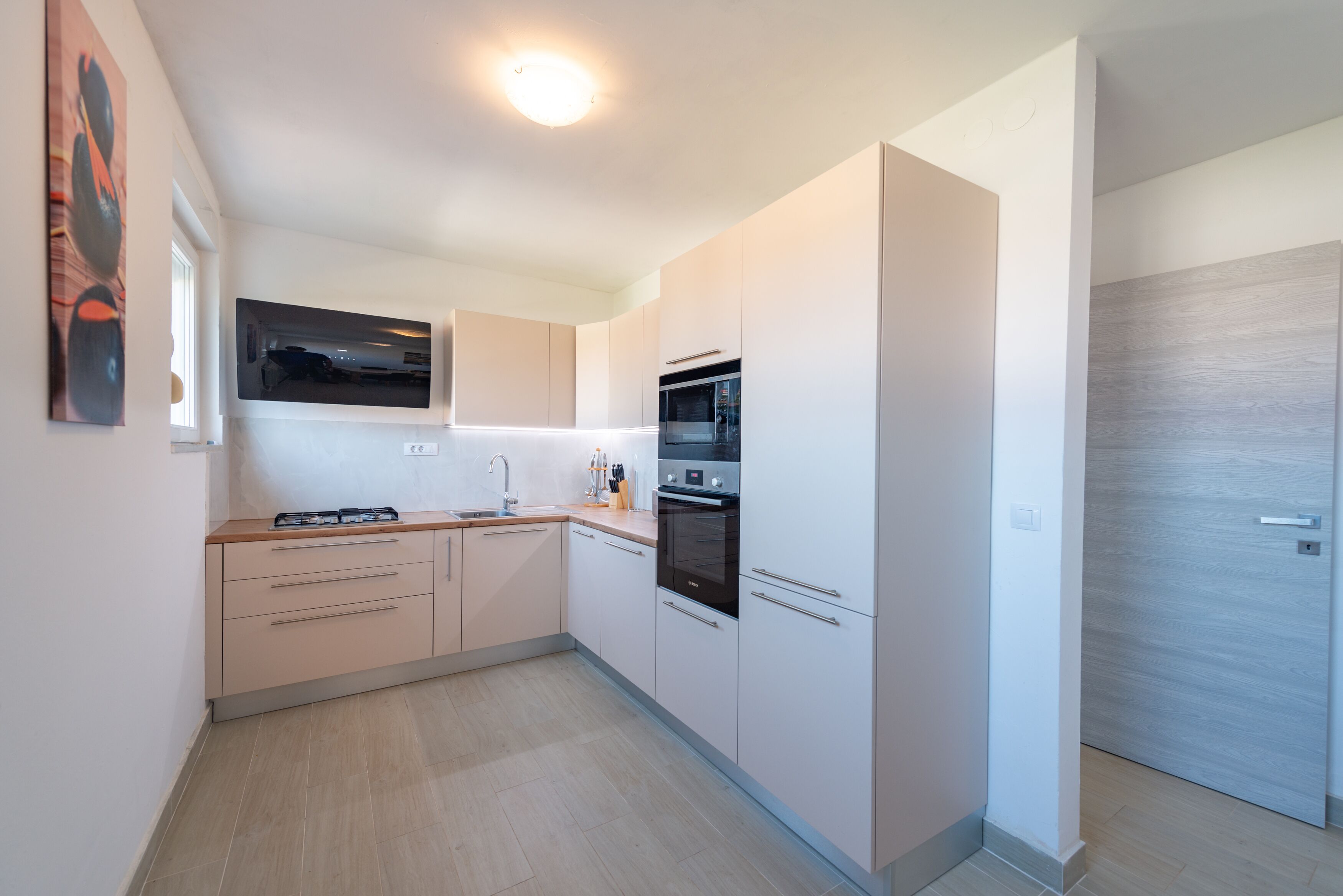 Una cucina moderna con mobili bianchi, forno integrato e un'ampia finestra sopra il lavello.