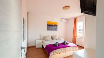Una camera da letto con un letto, un comodino, una TV a parete, una finestra con tende e un quadro appeso al muro.