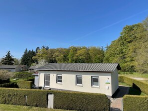 A small, single-story building with a tiled roof, surrounded by well-maintained hedges and trees.