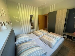 A bedroom with two beds, striped bedding, a mirror, and a wardrobe.