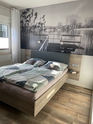 A modern bedroom with a large bed, a wooden headboard, and a mural of a lakeside scene.
