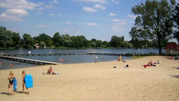 Ein Strand mit einer Anlegestelle, Menschen beim Schwimmen und einem klaren Himmel.