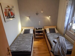 A small, cozy room with two single beds, a nightstand with a lamp, and a wall-mounted shelf. - Holiday house Geers am Klostersee Dargun - Holiday home Geers (Dargun)