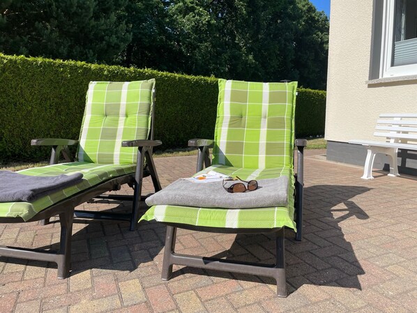 Two outdoor lounge chairs with green and white checkered cushions, a pair of sunglasses, and a book on one of the chairs.