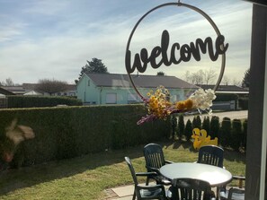A welcome sign with a circular frame, a table with chairs, and a hedge in a residential setting. - Holiday house Geers am Klostersee Dargun - Holiday home Geers (Dargun)