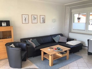 Een woonkamer met een zwarte leren bank, een houten salontafel en een kast met glazen deuren.