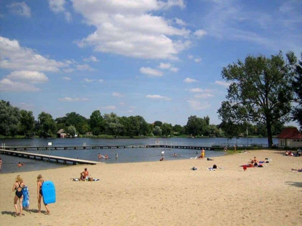 A beach with a dock, people swimming, and a clear sky.