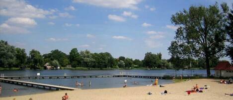 A beach with a dock, people swimming, and a clear sky.