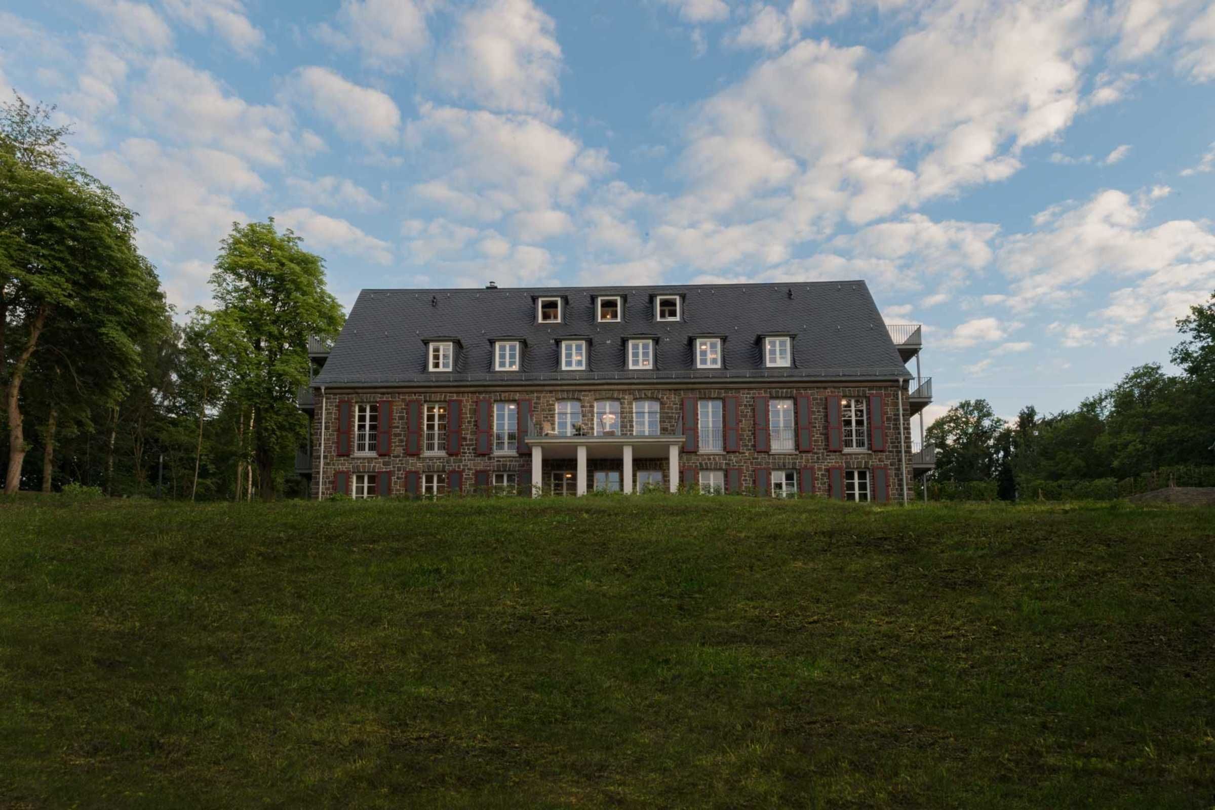 Un grand bâtiment historique à la façade symétrique, doté de nombreuses fenêtres et d’une entrée centrale flanquée de colonnes.