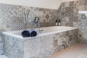 A bathroom with a patterned tile wall, a bathtub, and two rolled towels on the edge. - Apartment 11 - Edersee time out (Edertal)