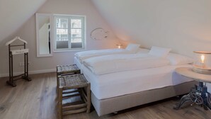 Een slaapkamer met een bed, een klein tafeltje met een lamp, een stoel, een kledingrek en een raam.