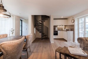 Eine moderne Küche mit Einbauofen, ein Essbereich mit Holztisch und Stühlen sowie eine Treppe, die in eine obere Ebene führt.