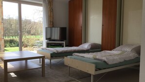 A room with two beds, a TV on a stand, a table, and a view of the outdoors. - Modern, quiet apartment in the countryside - in 30 minutes by train to Messe Frankfurt (Friedrichsdorf)
