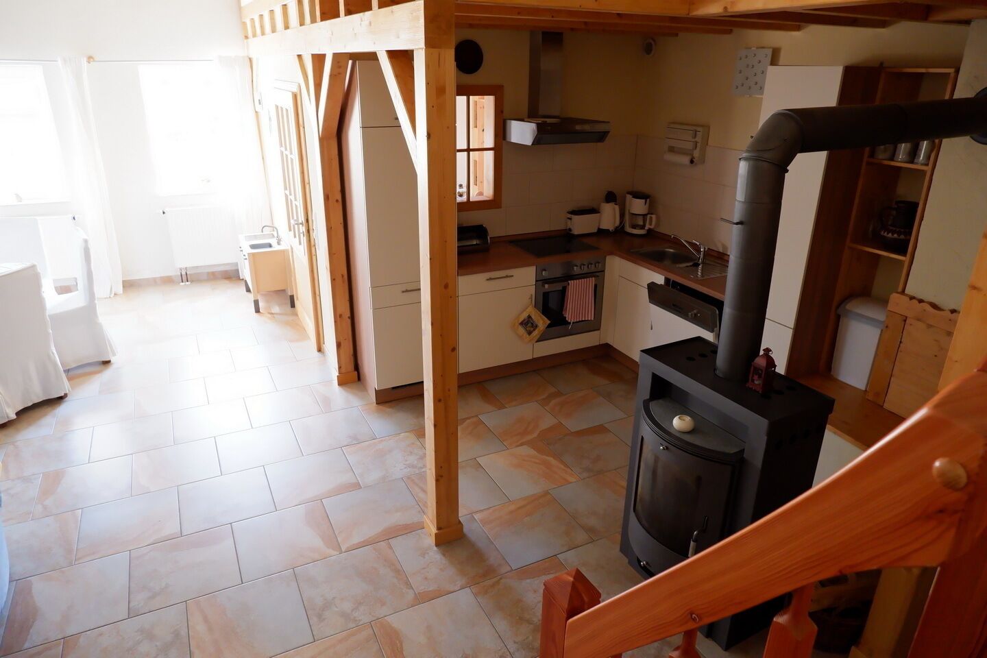A cozy kitchen with a wood-burning stove, a dining area with a wooden table, and a view of a bright room with a window.