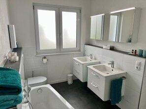 Moderni kylpyhuone, jossa on wc, kaksi pesuallasta, kylpyamme ja ikkuna.