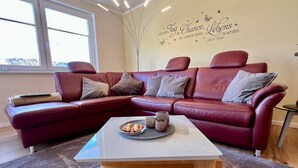 Ein Wohnzimmer mit einem roten Ledersofa, einem Holztisch und einer Wand mit einer dekorativen Schrift.
