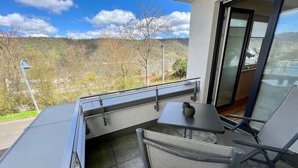 Ein Balkon mit Tisch und Stühlen, Blick auf die Landschaft und eine Tür zu einer Glastür.