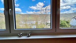 Ein Fenster mit zwei kleinen Vogelfiguren im Fensterbrett, mit Blick auf eine Landschaft mit Bäumen und einem entfernten Gebäude.