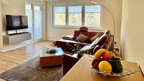 Ein modernes Wohnzimmer mit einem Flachbildfernseher, einem roten Sofa, einem Couchtisch und einer Obstschale.
