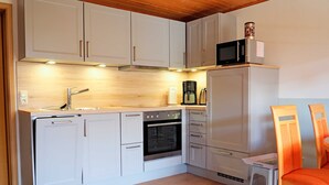 A compact kitchen with white cabinets, a built-in oven, a microwave, and a coffee maker. - Apartment "Schwansen" - Apartments on the holiday farm Jochimsen (Kappeln)