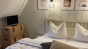 A neatly made bed with white and beige pillows, a white headboard, and a television on a wooden chest of drawers. - Beautiful vacation home "Svanvithe" - heated hot tub/sauna/WLan/fireplace (Glowe)