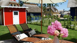 A red building with a white door, a thatched roof, and a white umbrella. - Beautiful vacation home "Svanvithe" - heated hot tub/sauna/WLan/fireplace (Glowe)