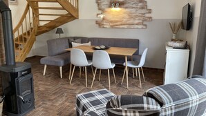 A cozy living room with a wooden staircase, a dining table with chairs, a sofa, and a fireplace. - Beautiful vacation home "Svanvithe" - heated hot tub/sauna/WLan/fireplace (Glowe)