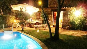 Piscina com escada, rodeada por um gramado e um edifício de pedra com guarda-sol.