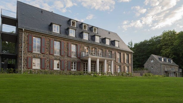 A large stone building with multiple windows and a balcony, surrounded by a well-maintained lawn. - Apartment 1 - Edersee time out (Edertal)