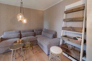 A modern living room with a sectional sofa, a wooden coffee table, a small side table, a wicker stool, and a built-in wooden shelf with books and decorative items. - Apartment 1 - Edersee time out (Edertal)
