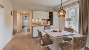 A modern kitchen with white cabinets, a central island, wicker chairs, and a hanging light fixture. - Apartment 1 - Edersee time out (Edertal)