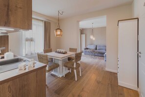 A modern kitchen with a dining area, wooden flooring, and a view into a living room with a sofa and a table. - Apartment 1 - Edersee time out (Edertal)