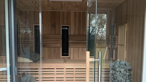 Un sauna avec des lambris en bois, un pilier en pierre et une porte en verre.