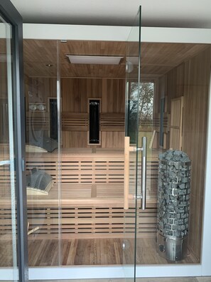 A sauna with wooden slats, a stone pillar, and a glass door.