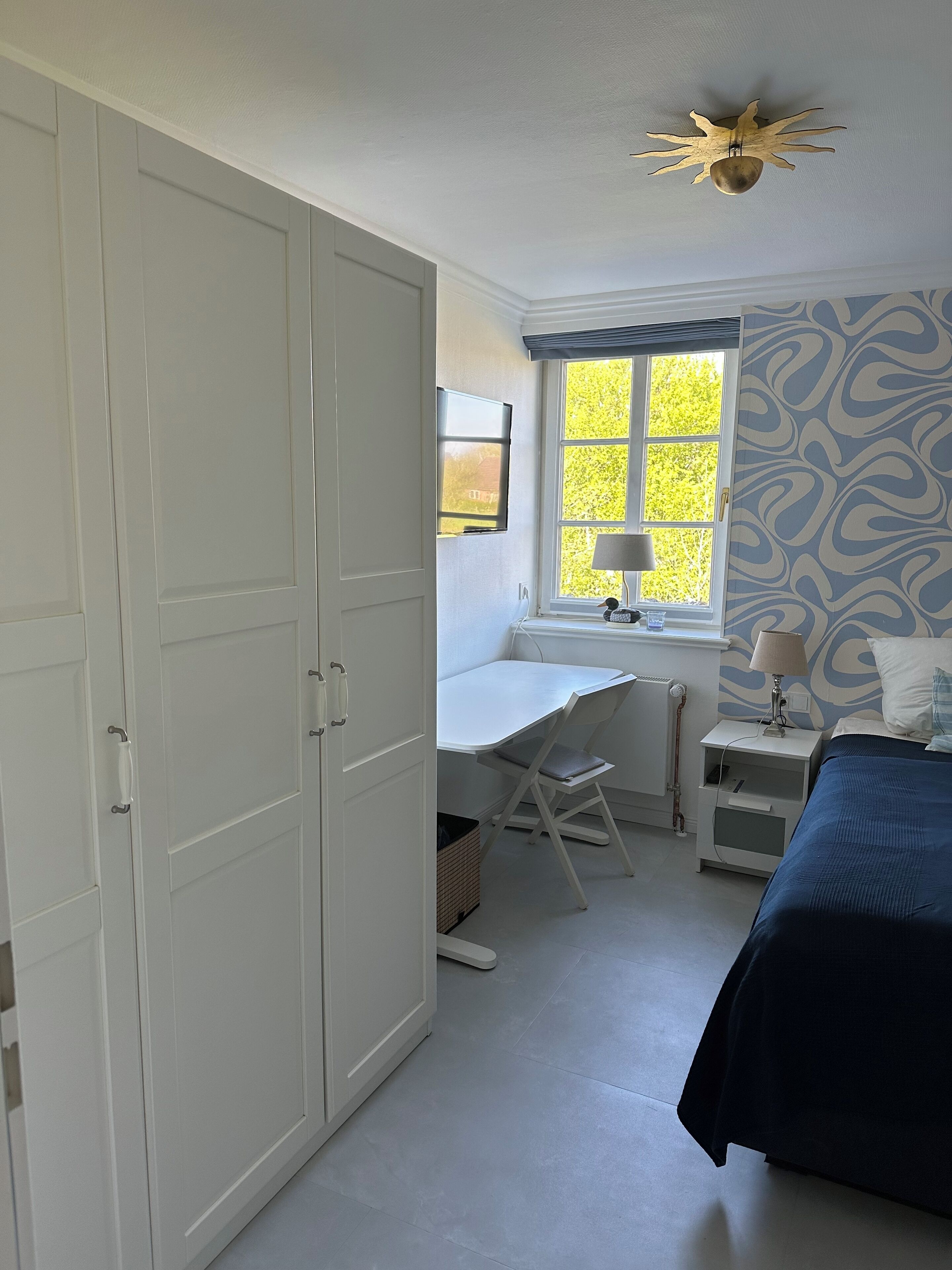 A bedroom with a bed, a desk, and a wardrobe.