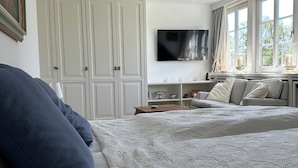Une chambre avec un grand lit, un téléviseur fixé au mur et une fenêtre avec des rideaux.